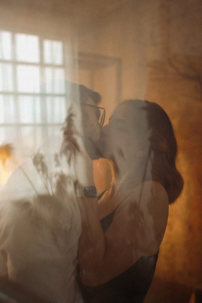 Mann und Frau küssen hinter einer Fensterscheibe